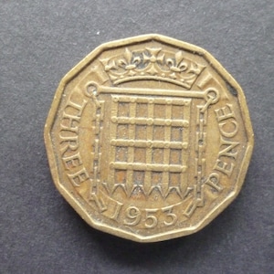 May include: A bronze-colored British three pence coin with the year 1953 and the words "THREE PENCE" around the edge.