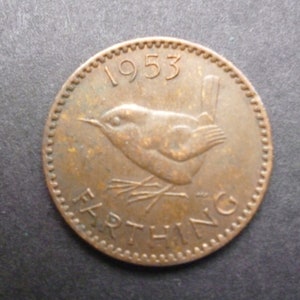 May include: A 1953 Farthing coin in a copper tone. The coin shows a bird design with the word "FARTHING" below and the year "1953" above. The coin has a textured edge and is set against a dark background.
