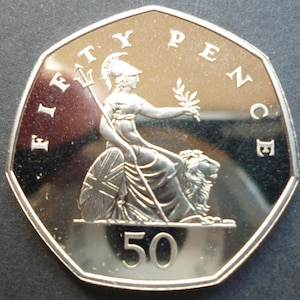 May include: A silver Fifty Pence coin depicting Britannia seated on a lion, holding a trident and olive branch. The coin is inscribed with "FIFTY PENCE" and the number "50".