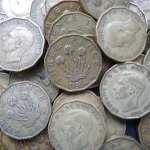 May include: A close-up of a pile of old British three pence coins. The coins are made of copper and have a design of a sprig of three thistles on the obverse. The coins are dated 1942 and 1944.