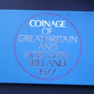 Peut inclure: Une boîte bleue avec des lettres argentées qui disent "Coinage of Great Britain and Northern Ireland 1977". Le texte est dans un cercle avec les mots "Specially struck at the Royal Mint to commemorate the Silver Jubilee of Her Majesty Queen Elizabeth II 1952-1977 - Containing a Crown Piece" autour de l'extérieur.
