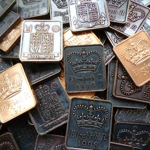 May include: A collection of square metal commemorative coins. The coins feature a crown design and the text "Elizabeth R" along with the year. Some coins have the Royal Mint logo. The coins are in various metallic colors.