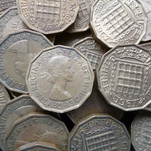 May include: A close-up of a pile of old British three pence coins. The coins are silver in color and have a design of a gate with bars on them. The coins are dated 1961 and 1963.