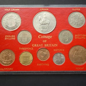 Op de afbeelding: Een 1953 muntenverzameling van Groot-Brittannië in een doorzichtige plastic houder met een rode achtergrond. De collectie bevat een half crown, crown, florin, Engelse shilling, Schotse shilling, threepence, farthing, sixpence, halfpenny en een penny.