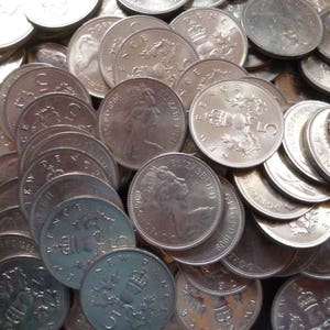 Puede incluir: Una colección de monedas británicas de plata con el perfil de la reina Isabel II. Las monedas están dispuestas en un patrón aleatorio, con algunas monedas apiladas unas sobre otras.