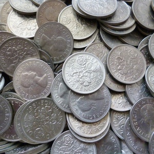 Puede incluir: Primer plano de una pila de monedas de seis peniques británicas de plata. Las monedas muestran el perfil de la reina Isabel II y la inscripción "SIX PENCE" junto con el año de acuñación.
