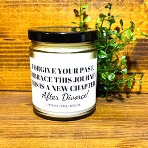May include: A white candle in a glass jar with a black lid. The candle has a white label with the text "FORGIVE YOUR PAST, EMBRACE THIS JOURNEY, THIS IS A NEW CHAPTER After Divorce!"