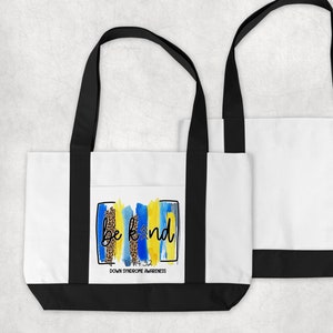 May include: White tote bag with black handles and a blue, yellow, and black graphic that says "Be Kind" with the text "3-21 Down Syndrome Awareness" below.