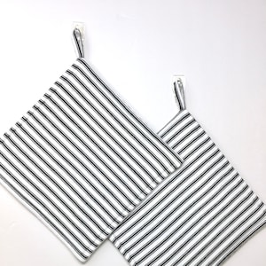 May include: Two black and white striped kitchen pot holders hanging on hooks. The pot holders are made of cotton fabric and have a simple design.