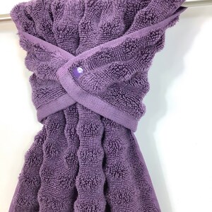 May include: A purple terry cloth towel with a button closure. The towel is hanging on a silver towel rack.