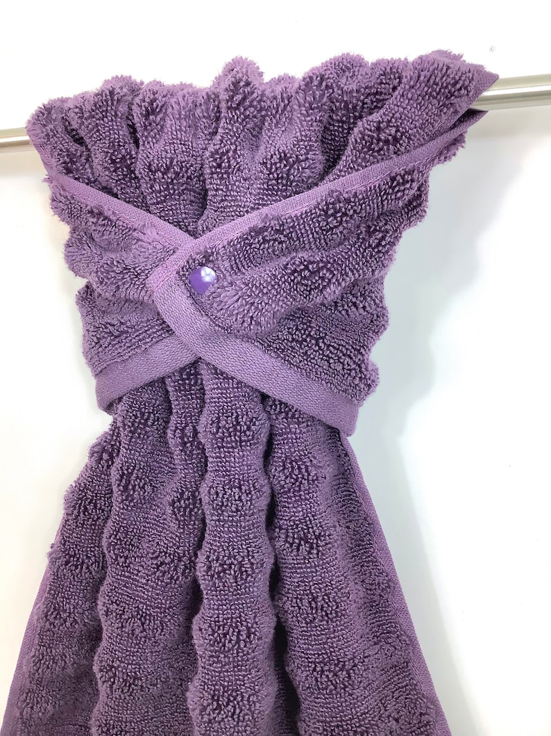 May include: A purple terry cloth towel with a button closure. The towel is hanging on a silver towel rack.