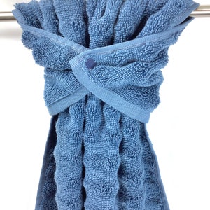 May include: A blue bath towel with a button closure is hanging on a towel rack.
