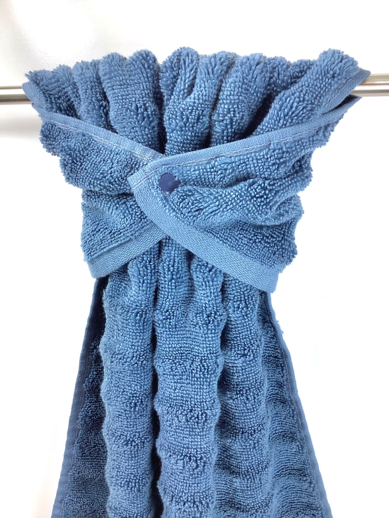 May include: A blue bath towel with a button closure is hanging on a towel rack.