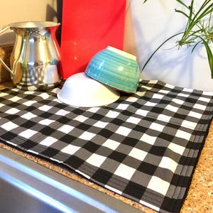 May include: Black and white checkered kitchen dish drying mat with two bowls on top. The bowls are white and turquoise.
