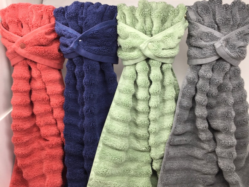 May include: Four kitchen towels hanging on a rack. The towels are in different colors: coral, navy blue, light green, and gray. The towels have a textured, waffle-like pattern.