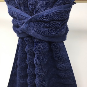 May include: A dark blue, textured, cotton towel with a button closure. The towel is hanging on a silver towel bar.