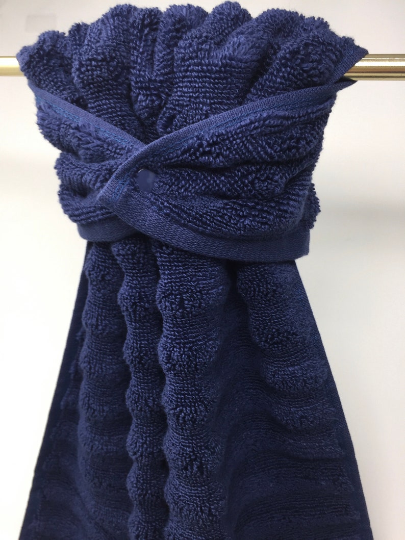 May include: A dark blue, textured, cotton towel with a button closure. The towel is hanging on a silver towel bar.
