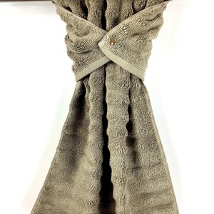 May include: A brown kitchen towel with a textured pattern is hanging on a silver towel rack. The towel has a button closure.