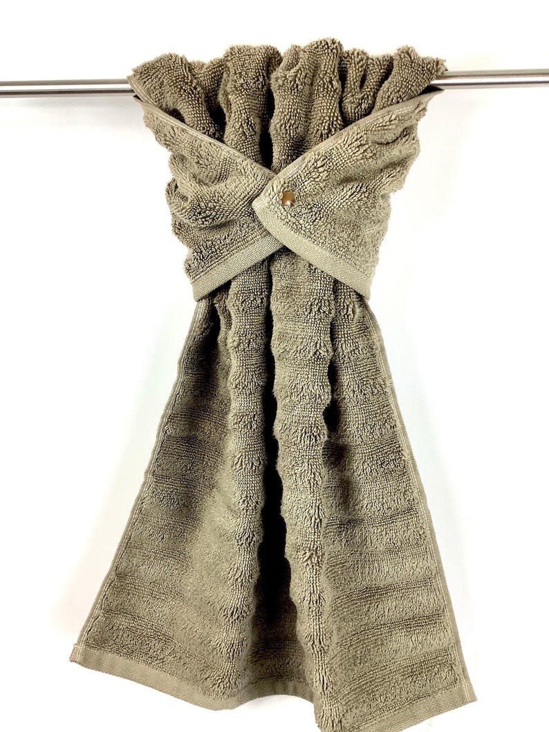 May include: A brown kitchen towel with a textured pattern is hanging on a silver towel rack. The towel has a button closure.