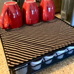 May include: A black and white striped fabric coffee pod holder with three red mugs and a black and silver metal frame.