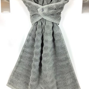 May include: A gray kitchen towel with a button closure hangs on a silver towel rack. The towel is made of a soft, absorbent material and is perfect for drying dishes or hands.