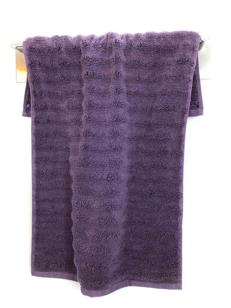 May include: A purple bath towel hanging on a silver towel rack.