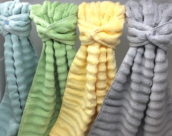 May include: Four bath towels hanging on a rack. The towels are green, yellow, gray, and blue. The towels are all folded in a similar way, with the ends tucked in and the middle part hanging down.