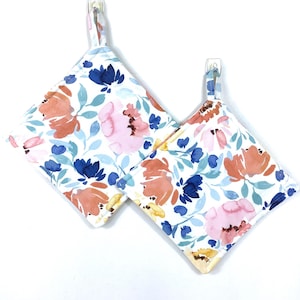 May include: Two floral print pot holders with a white background and a blue, pink, and orange floral pattern. The pot holders have a loop for hanging.