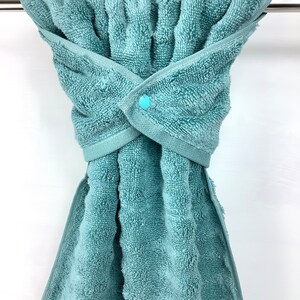 May include: A teal blue towel with a snap closure hanging on a silver towel rack.