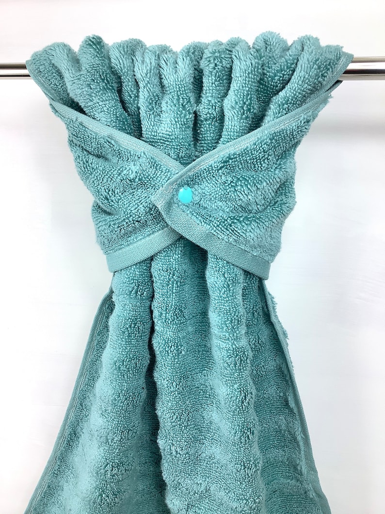 May include: A teal blue towel with a snap closure hanging on a silver towel rack.