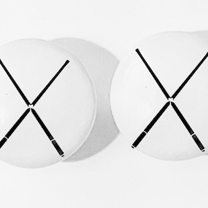May include: Two white round coasters with a black X design. The X is formed by two crossed lines.