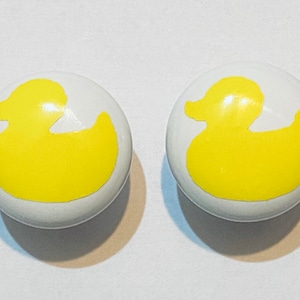 May include: Two white ceramic knobs with yellow rubber ducky silhouettes.