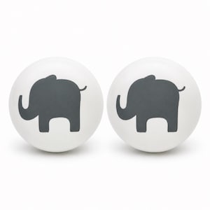 May include: Two round, white ceramic knobs, each featuring a dark gray silhouette of an elephant facing left. The knobs have a smooth, spherical surface and a clean, simple design, providing a functional and decorative element for furniture.