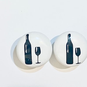 May include: Two white ceramic knobs with black silhouettes of a wine bottle and glass.