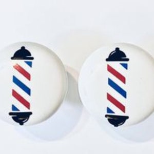 May include: Two white round buttons with a red, white, and blue barber pole design. The barber pole is a traditional symbol of a barbershop.