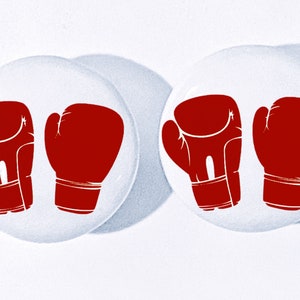 May include: Two circular white pin-back buttons, each featuring a graphic illustration of a pair of red boxing gloves. The design is identical on both buttons, showcasing the gloves side-by-side in a bold, solid red color against the white background.