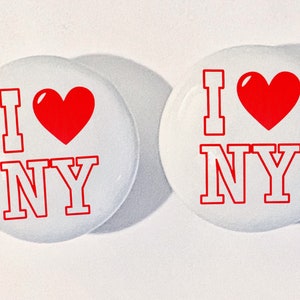 May include: Two white round buttons with red text and a red heart. The text on the buttons reads "I love NY".