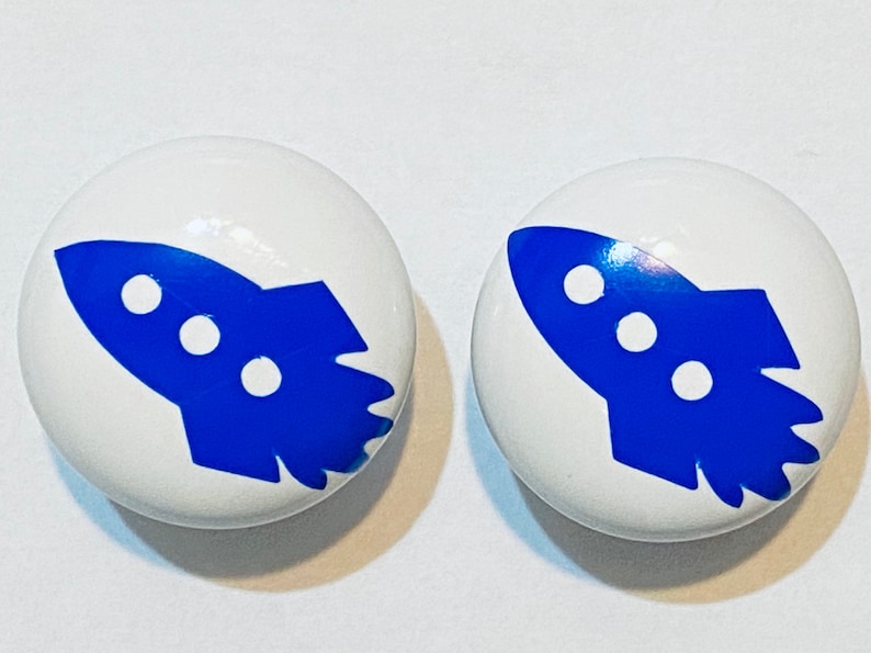 Może przedstawiać: Dwa białe ceramiczne pokrętła z niebieskimi wzorami rakiet. Rakiey mają trzy białe k&oacute;łka.