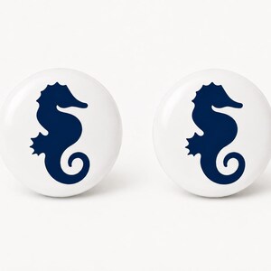 May include: Two round white ceramic knobs, each featuring a dark navy blue seahorse silhouette printed in the center. The knobs have a smooth, glossy finish and a circular shape, providing a clean and simple design for furniture hardware.