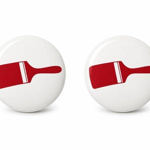 May include: Two circular white pin-back buttons, each featuring a centered graphic of a red paintbrush with a white stripe on the handle. The design is identical on both buttons, showcasing a clean, minimalist aesthetic with a glossy finish.