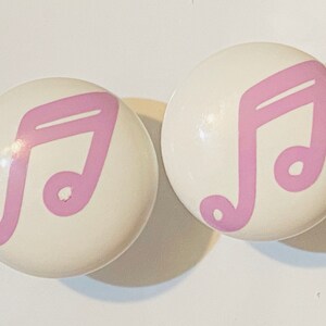 May include: Two white ceramic drawer knobs with pink musical note designs.