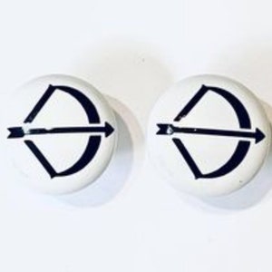 May include: A pair of white round buttons with a black bow and arrow design.