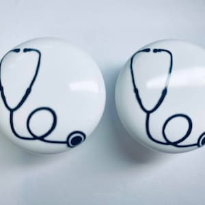 May include: Two white ceramic cabinet knobs with a black stethoscope design.