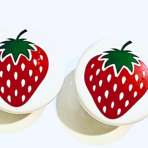 May include: Two white ceramic knobs with a red and green strawberry design.