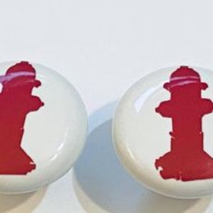 May include: Two white ceramic knobs with a red fire hydrant design. The knobs are round and have a smooth surface.