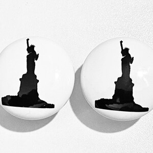 May include: Two white ceramic knobs with a black silhouette of the Statue of Liberty.