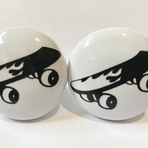 May include: Two white ceramic knobs with a black and white image of a skateboard with flames on the side.