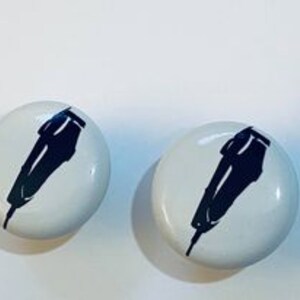 May include: Two white round buttons with a black silhouette of an electric razor on each.