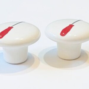 May include: Two white ceramic drawer knobs with a red screwdriver design.