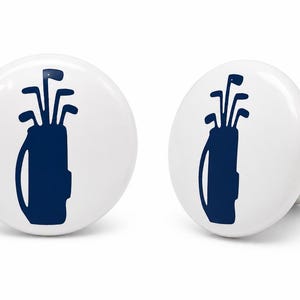 May include: Two round white cabinet knobs featuring a dark blue graphic print of a golf bag filled with golf clubs. The knobs have a smooth, glossy finish and a cylindrical base, presented from both a front-facing and a side-angled perspective.
